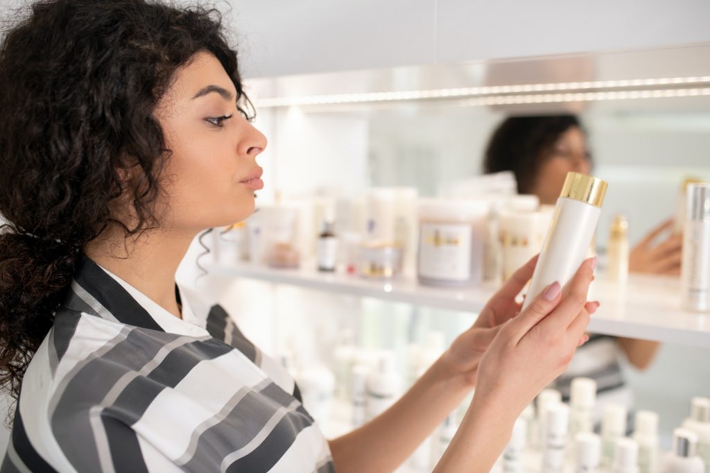 Dark-haired beautiful woman in striped shirt choosing facial cream